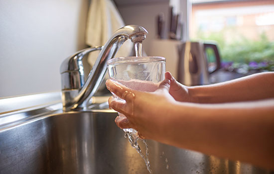 close-up of child's arms filling a glass of water under a kitchen faucet