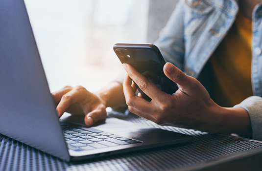 person holding phone while using laptop