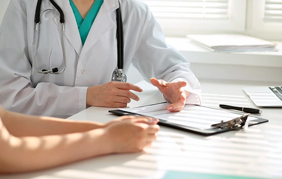 Doctor in white coat and stethoscope discussing medical notes with patient at desk during consultation