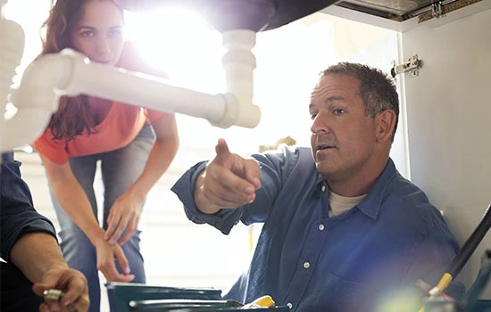 Plumber instructing a child on pipe installation work under a sink, demonstrating hands-on plumbing skills and mentorship