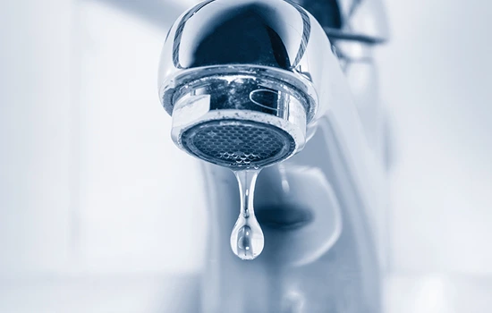 Water dripping from a chrome faucet aerator with a blurred background