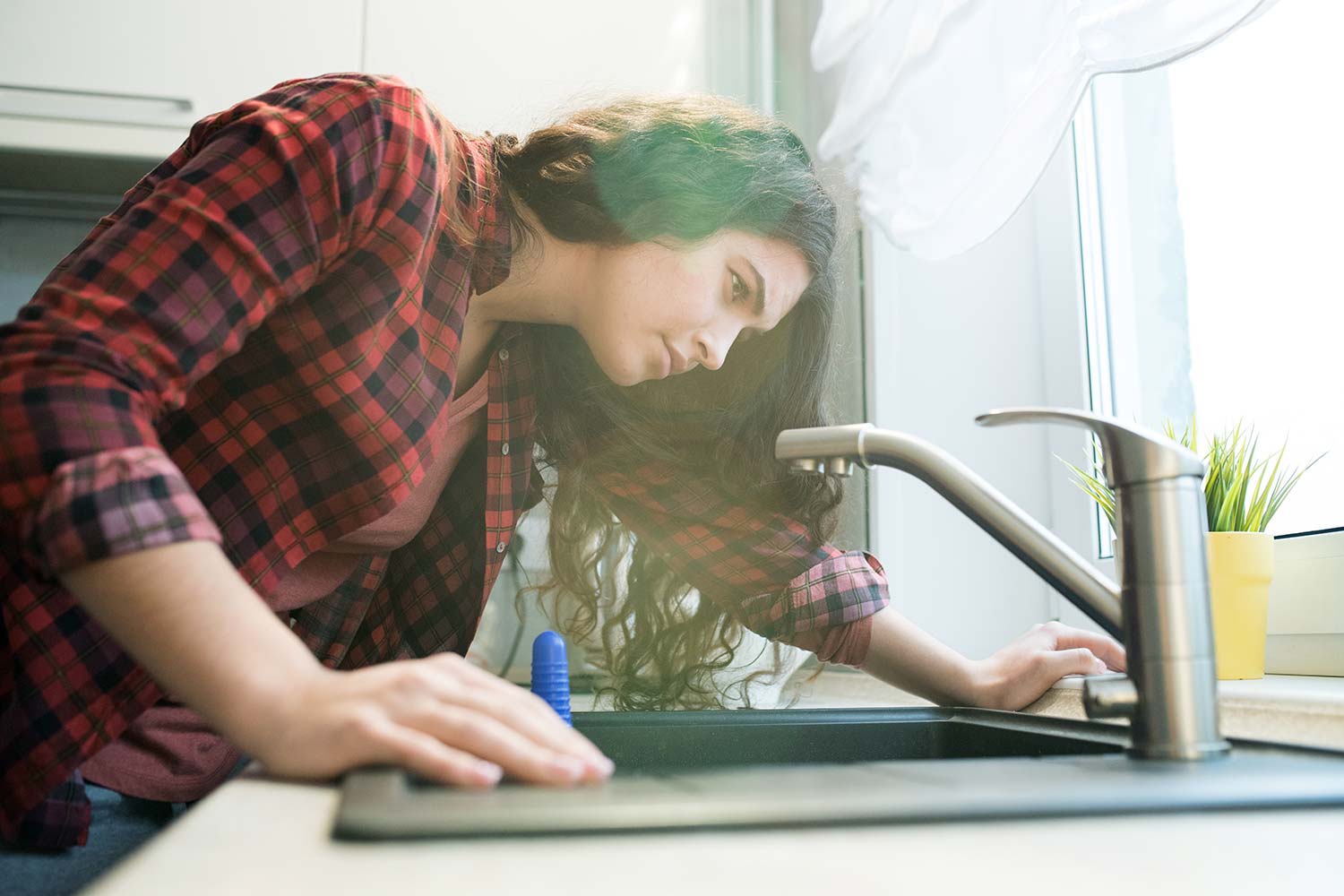 young woman checking kitchen faucet for leaks