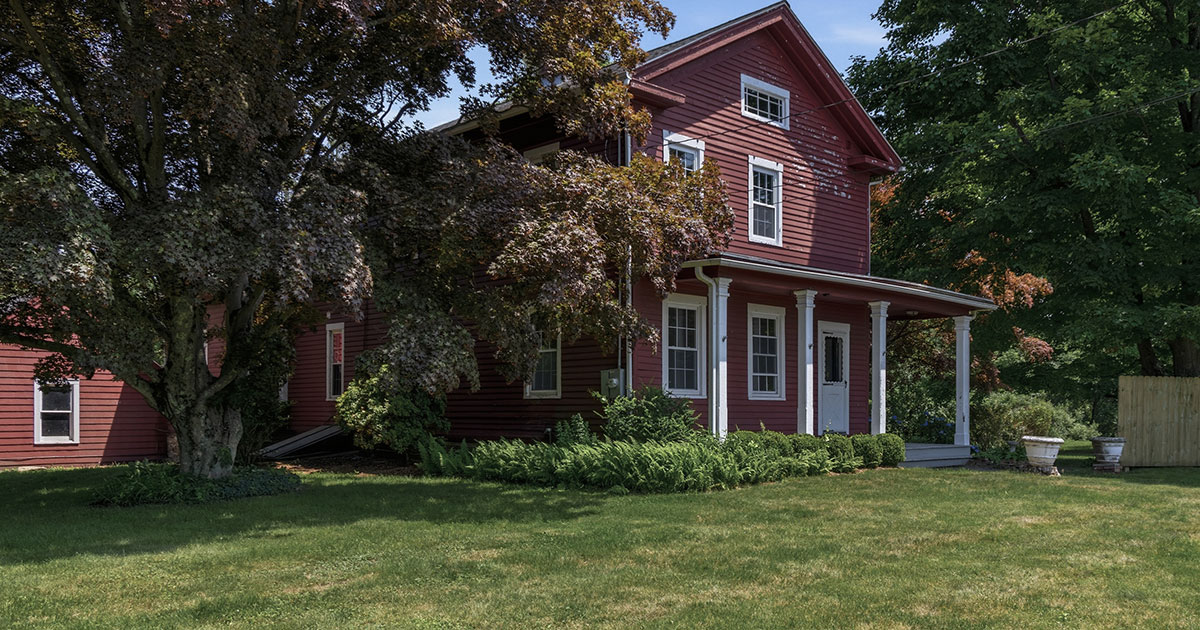 238-isinglass-road-shelton-ct Large red two-story farmhouse-style home with white trim and a covered front porch, partially shaded by an old tree